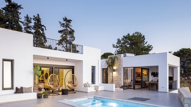 Ein modernes Haus mit Pool, Sitzgelegenheiten im Freien und einer Steinmauer.