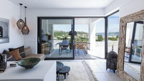 Ein modernes Wohnzimmer mit einer Couch, einem Esstisch und einem großen Fenster mit Blick ins Freie.