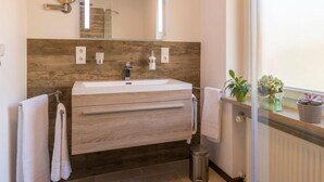 Un bagno moderno con un mobile lavabo in legno, uno specchio grande e una finestra con piante in vaso.