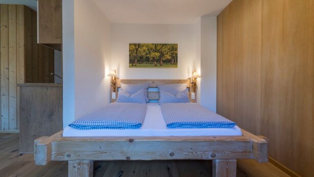 Un letto matrimoniale con cornice in legno, due comodini con lampade e un quadro raffigurante alberi appeso al muro.