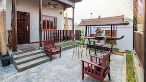 A courtyard with a wooden bench, a table, and chairs. There are steps leading to a door and a small garden area. - Teko Island (Siem Reap)