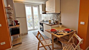 A compact kitchen with a dining area, a built-in shelf unit, and a view through a glass door. - GarbaStop (Rome)