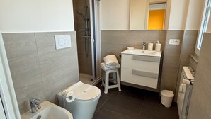 A modern bathroom with a shower, toilet, bidet, sink, and a mirror above the sink. - GarbaStop (Rome)