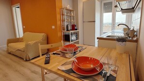 A compact living space with a dining area, a sofa, a kitchen with a window, and a built-in shelf unit. - GarbaStop (Rome)