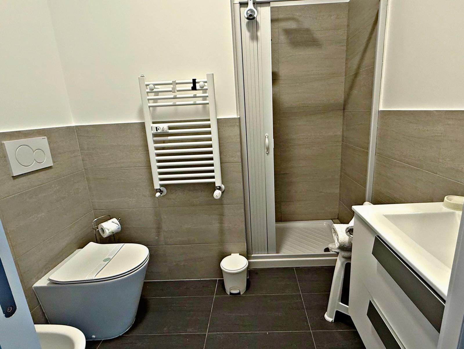 Casa de banho com sanita, bidé, chuveiro e um porta-toalhas.