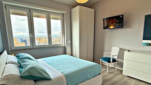 A bedroom with a bed, a chair, a TV, and a wardrobe. - GarbaStop (Rome)