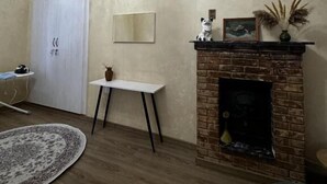Ein Zimmer mit Kamin, einem weißen Tisch, einem kleinen Teppich und einer Tür, an der ein Handtuch hängt.