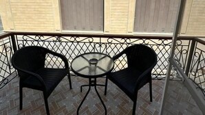 Ein Balkon mit zwei schwarzen Stühlen und einem kleinen runden Tisch, mit Fliesenboden und Metallgeländer.
