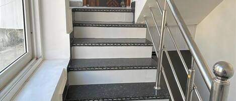 En trappe med sorte marmortrin og gelænder i metal, som fører op til en dør med et geometrisk mønster.