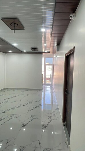Um corredor com piso de mármore brilhante, teto com iluminação embutida e uma porta à direita.