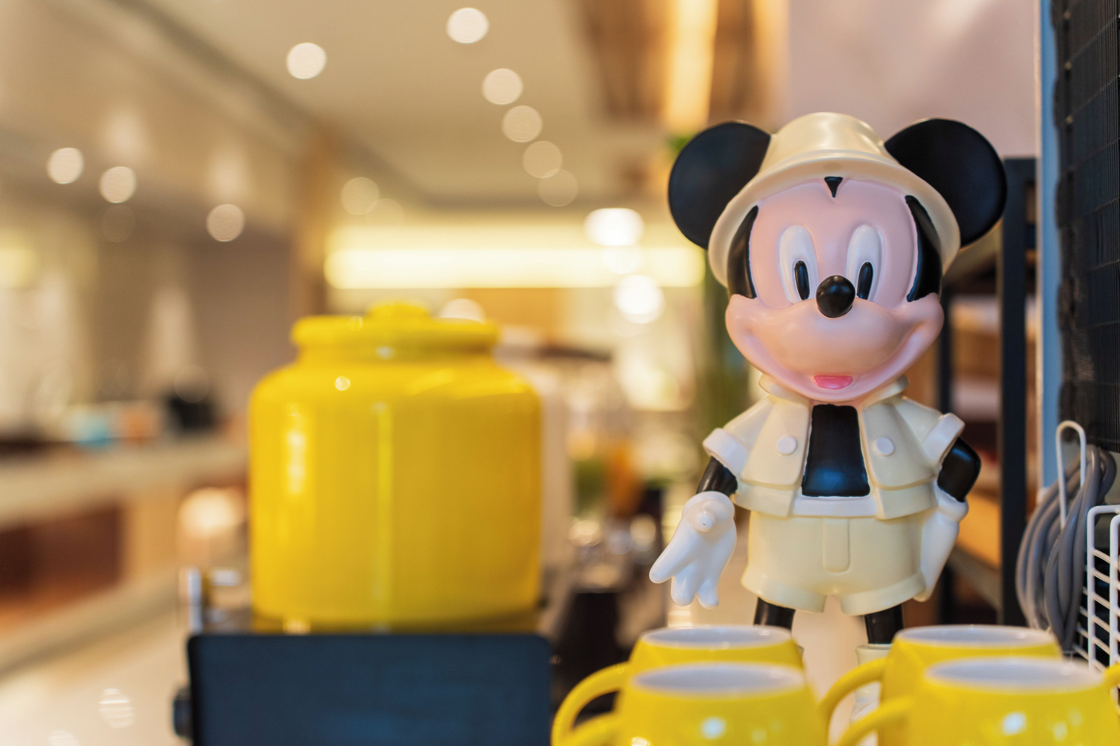 A figurine of a character in a safari outfit standing next to yellow mugs.