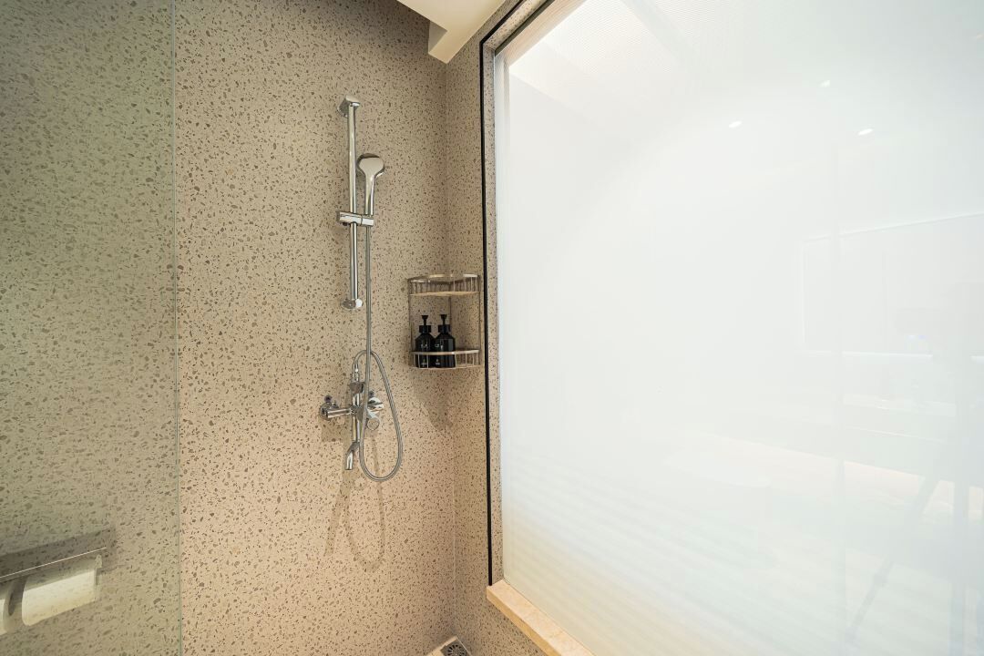 A bathroom with a shower, a glass door, and a shelf with toiletries.