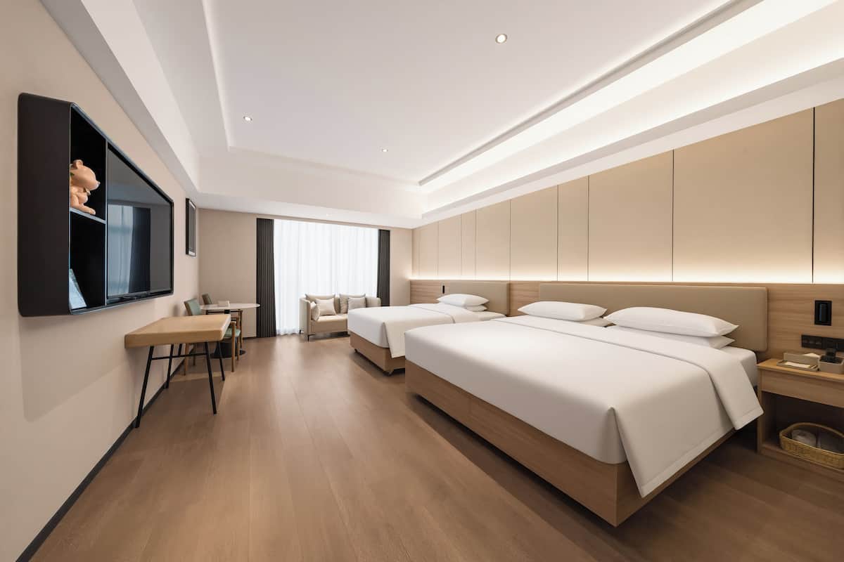 Quarto de hotel moderno com piso de madeira, duas camas, uma escrivaninha e uma TV fixada na parede.