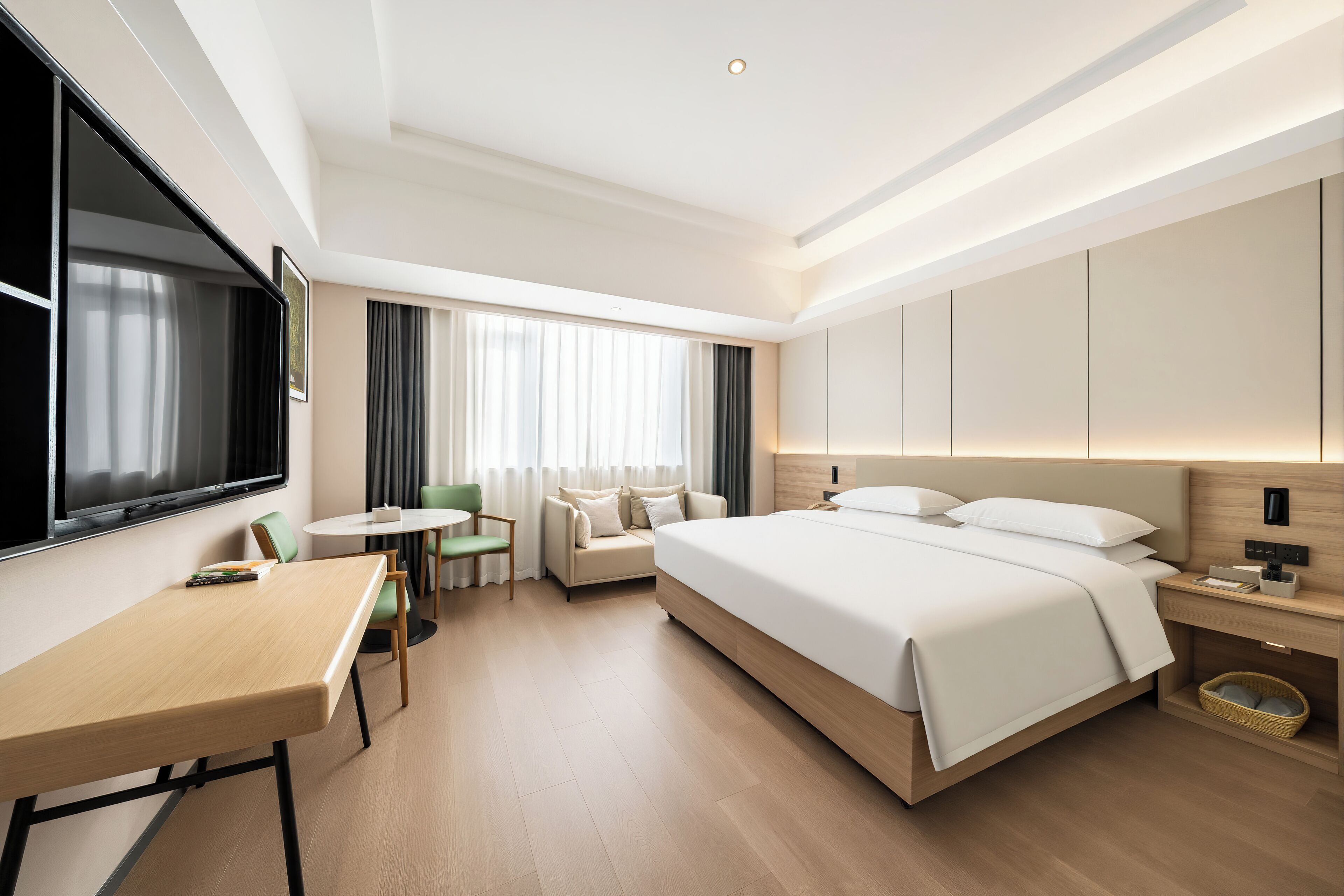 Ein modernes Hotelzimmer mit einem großen Bett, einem Schreibtisch, einem Sessel, einem kleinen Tisch und einem Fernseher.