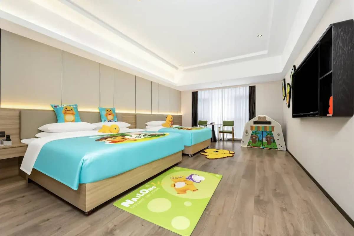 Quarto de hotel moderno com uma cama grande, mesas de cabeceira, uma escrivaninha e um espaço para brincar.