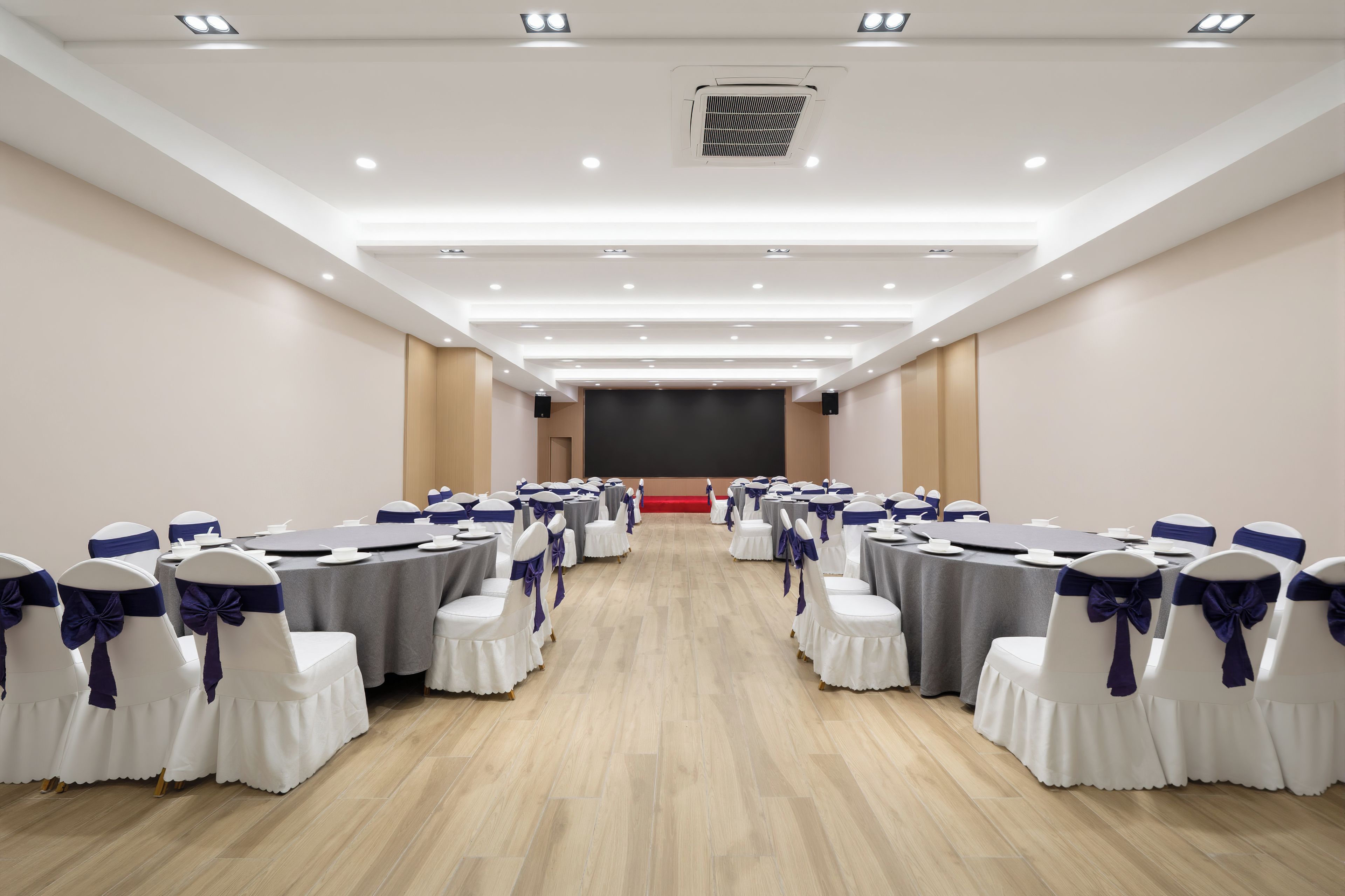 Une salle de conférence avec des rangées de tables et de chaises, une scène et un écran de projection.