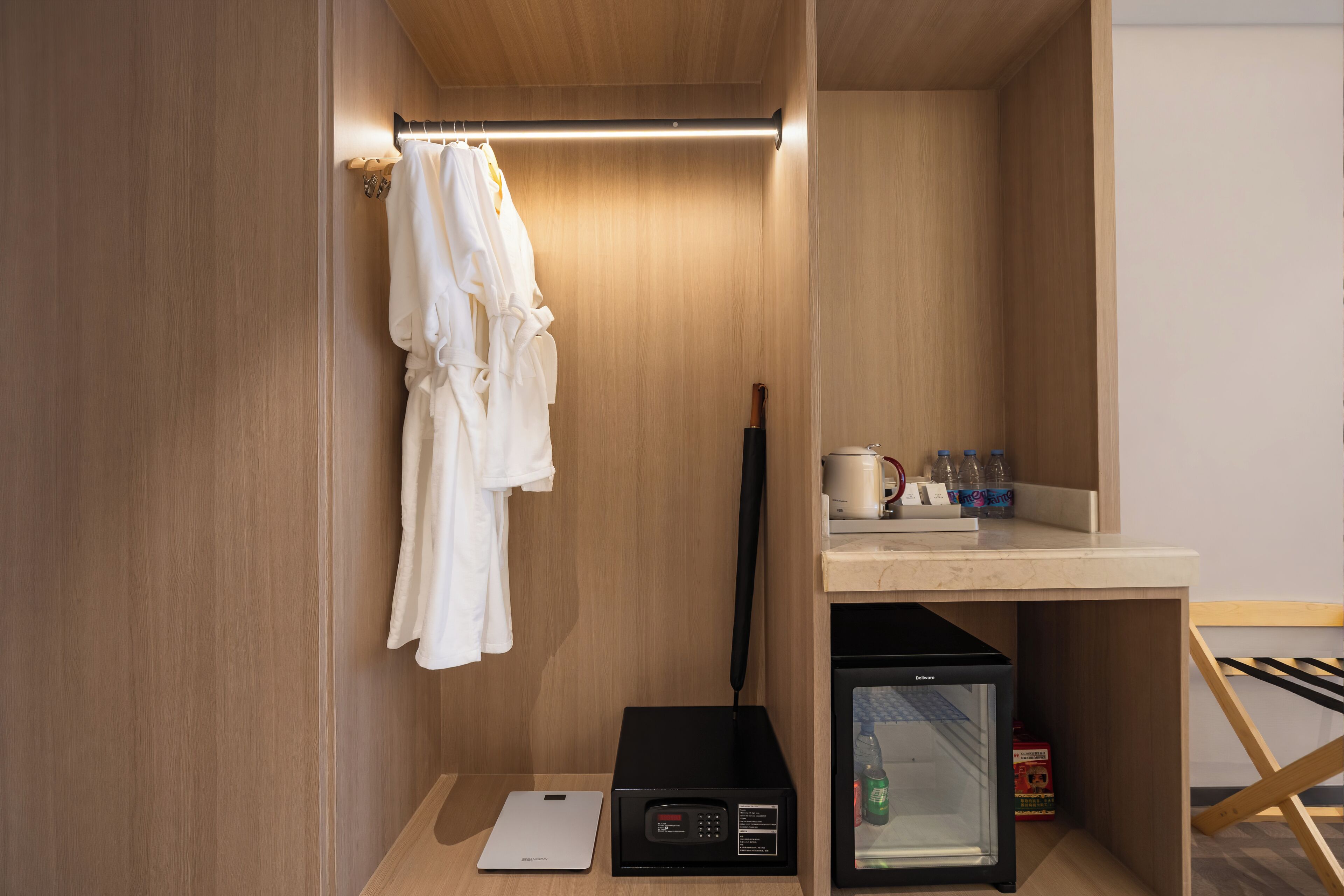 A compact hotel room with a wooden interior, a minibar, a microwave, a refrigerator, and a white robe hanging on the wall.