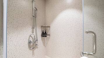 A shower area with a glass door, a wall-mounted handrail, and a shelf with toiletries.