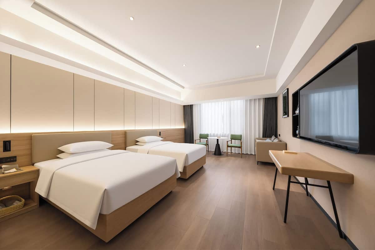Quarto de hotel moderno com duas camas, uma escrivaninha, uma cadeira e uma janela grande.