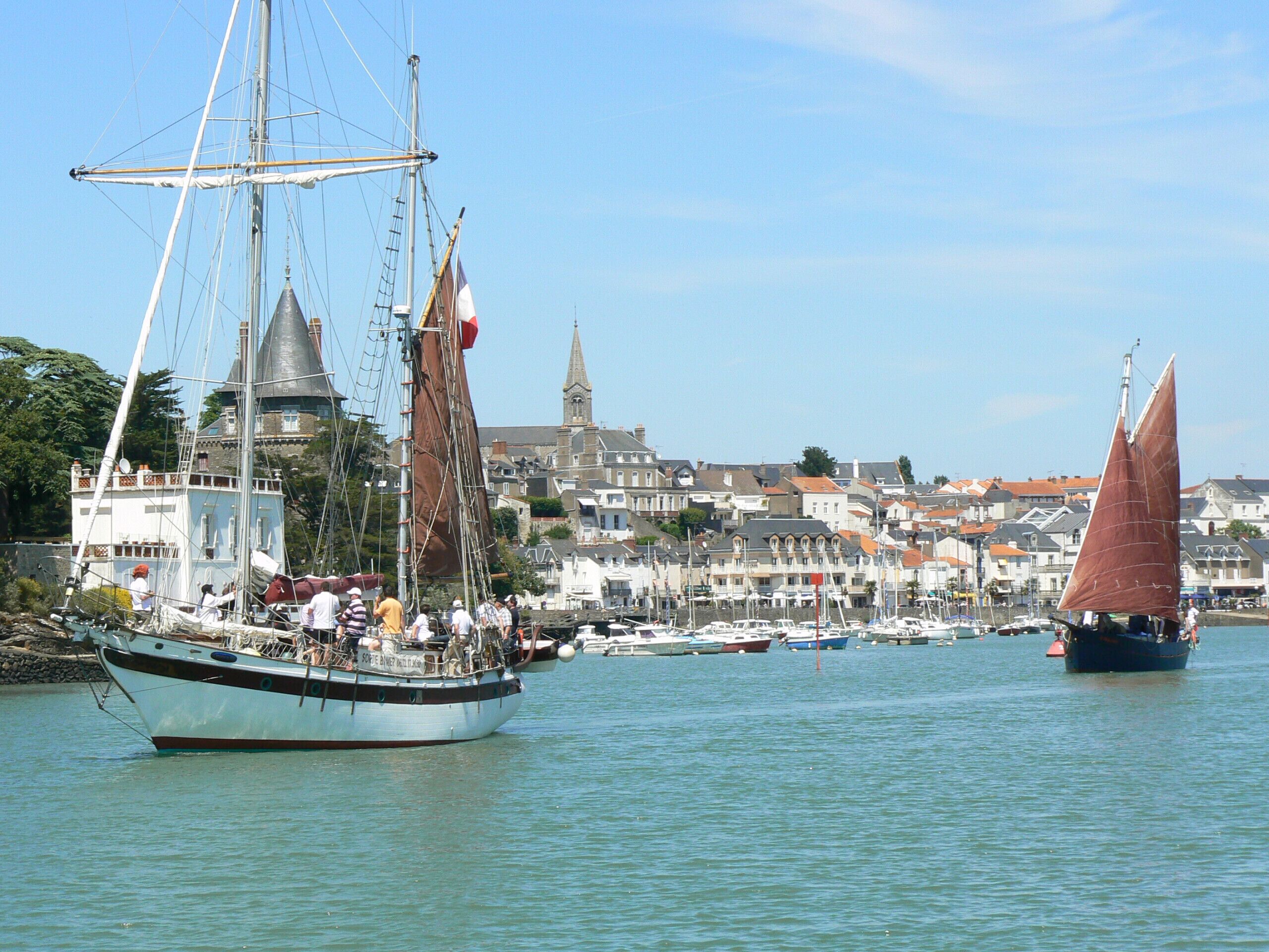 A harbor with sailboats, a historic building, and a densely packed town in the background.