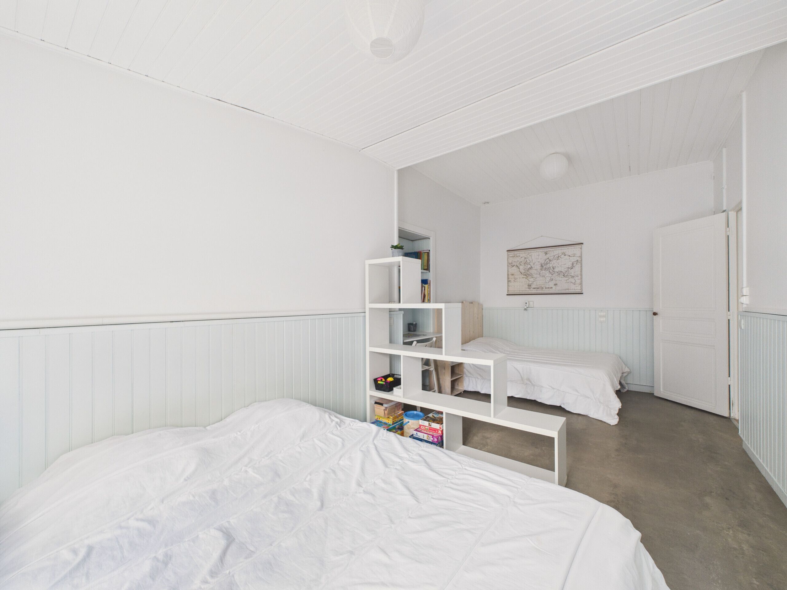 A bedroom with a large bed, a white wardrobe, a small desk, and a map on the wall.