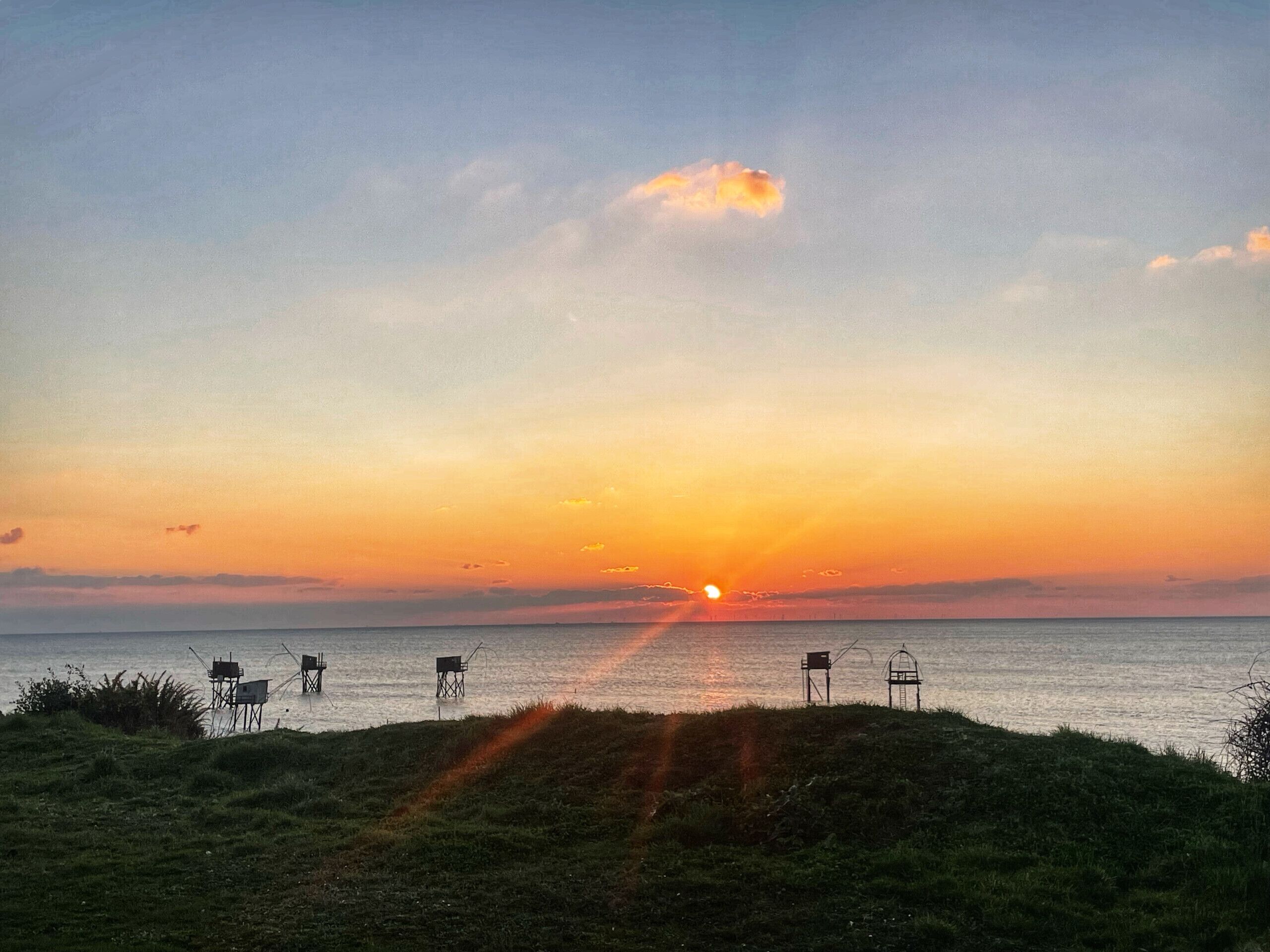 Ein Sonnenuntergang über einem Gewässer mit grüner Landschaft und mehreren auf Stelzen stehenden Gebäuden.