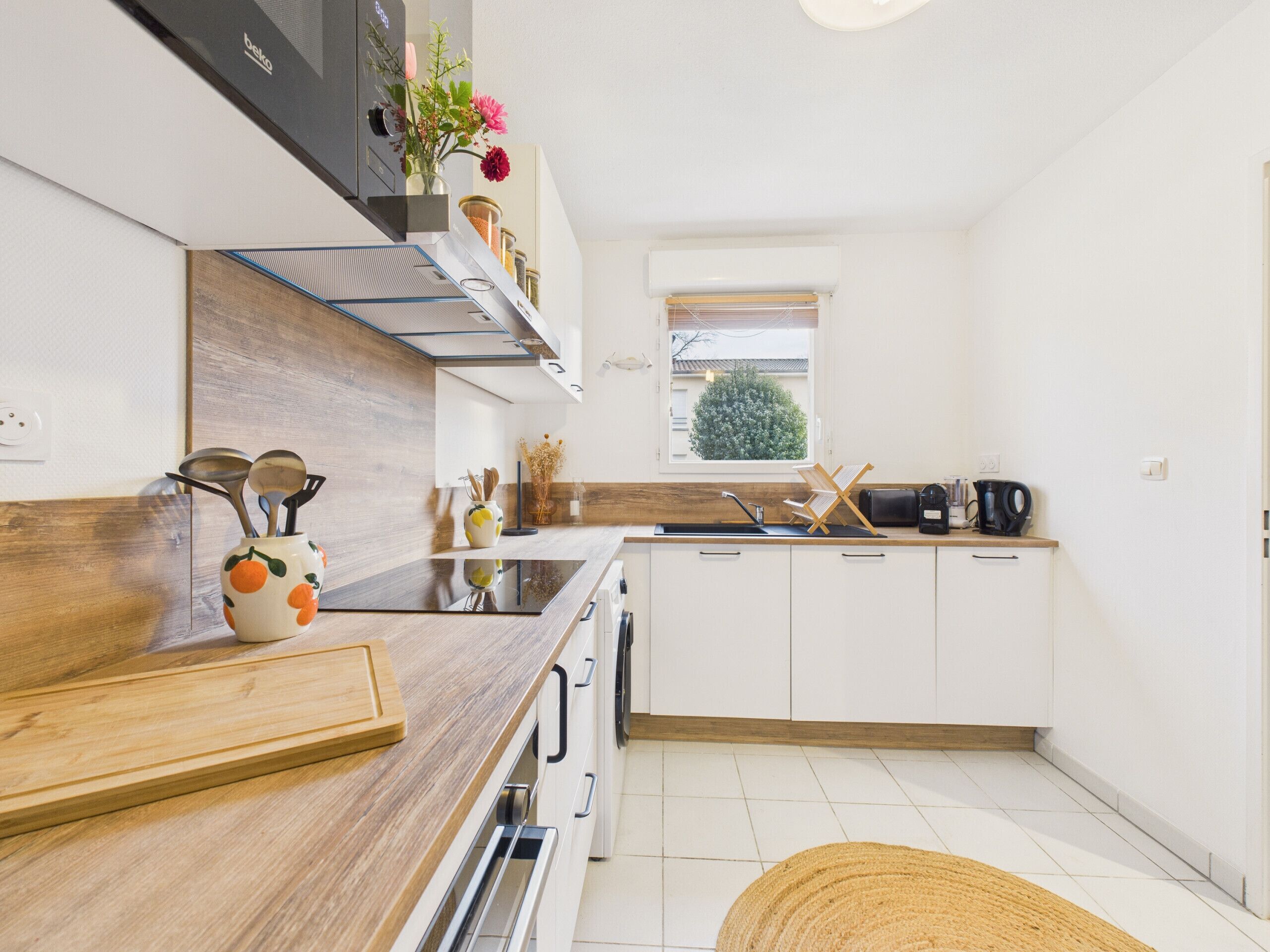 A modern kitchen with a wooden countertop, white cabinets, a built-in oven, and a window with a view of greenery.