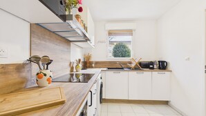 Una cocina moderna con encimera de madera, armarios blancos, horno integrado y ventana con vista a zonas verdes.