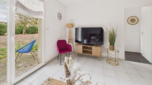 Una sala de estar con televisor, una silla roja, una silla azul, una lámpara de pie y una planta.