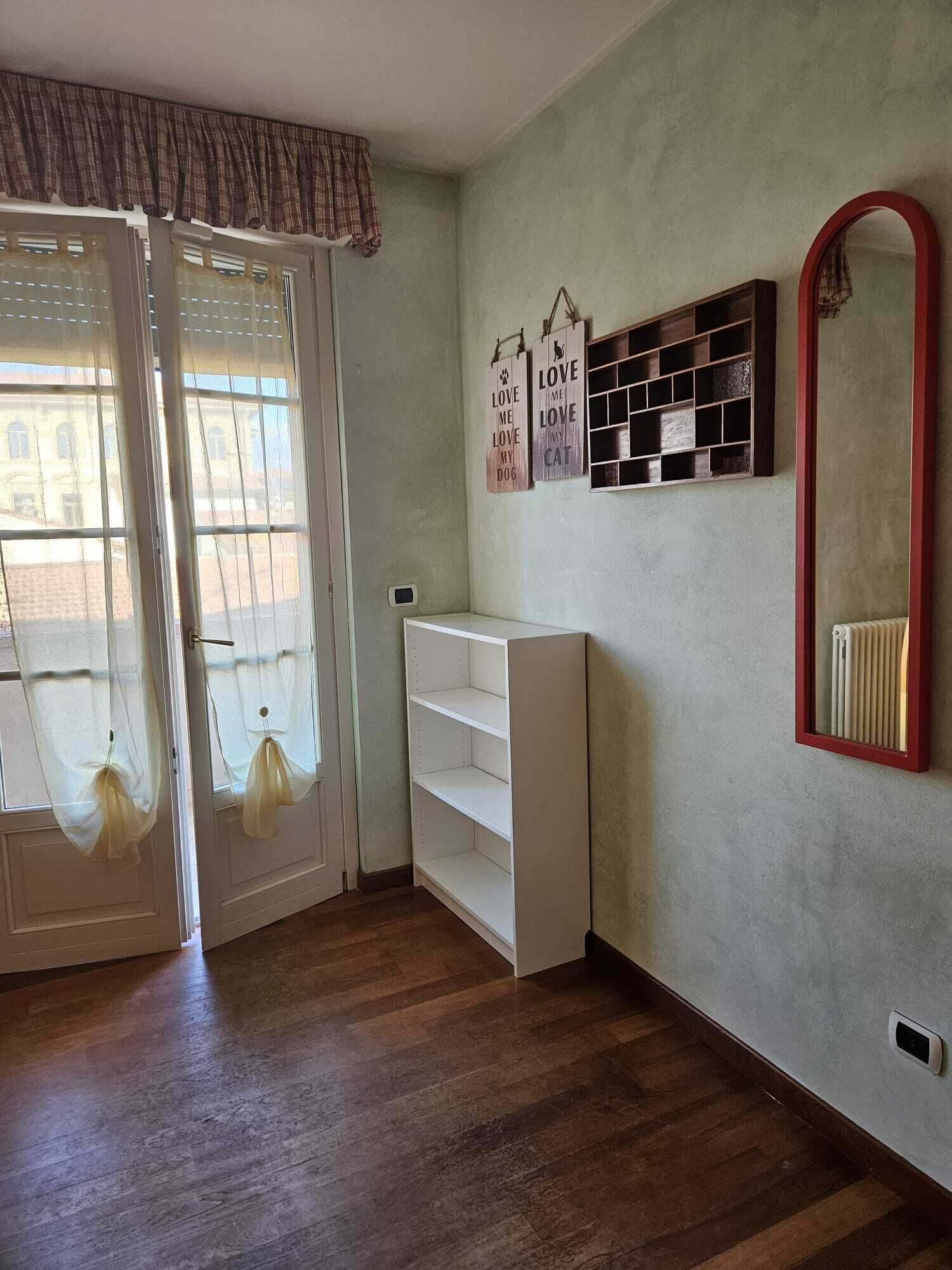 A room with a sliding glass door, a white shelving unit, a mirror with a red frame, and two wall decorations with dog and cat illustrations.