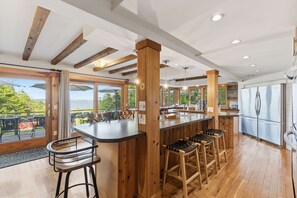 Una cocina con vigas de madera, una zona de bar con taburetes, ventanas amplias y un refrigerador.