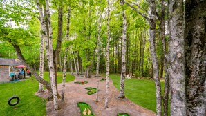 A forested area with a dirt path, green benches, and a tire swing. - Pine Lodge 11BR: Sleeps 34 - Group Getaway & Events (Northport)