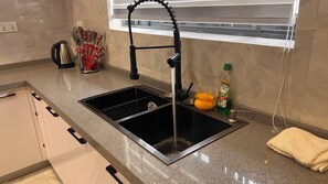 Una cocina con un lavamanos negro, una ventana sobre el lavamanos y una botella de detergente en la encimera.