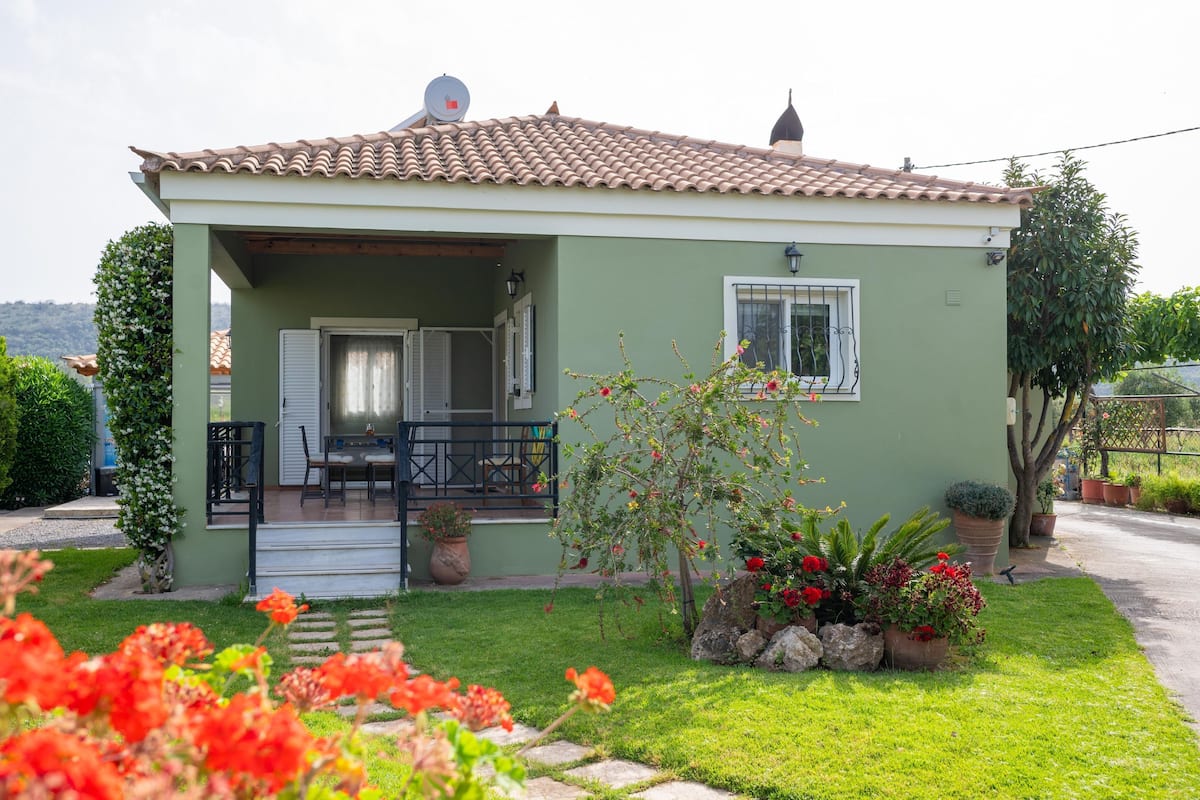 A single-story house with a tiled roof, a covered porch, and a small garden with potted plants and flowers.