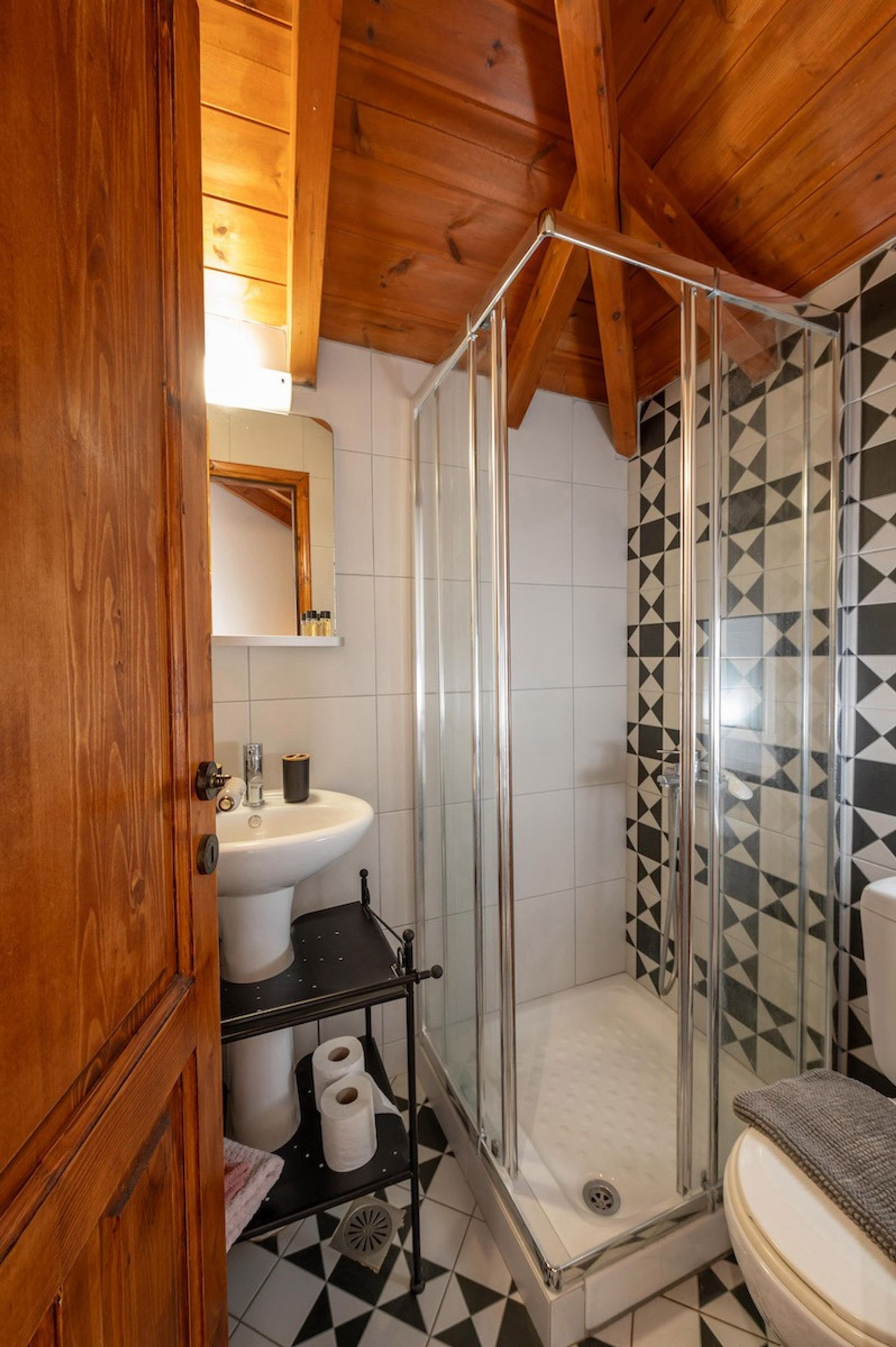 A wooden-framed bathroom with a glass shower enclosure, a sink, and a toilet.