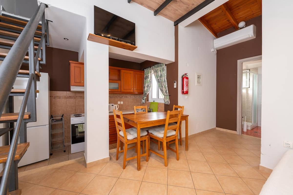A compact kitchen with a dining table and chairs, a small oven, and a refrigerator.