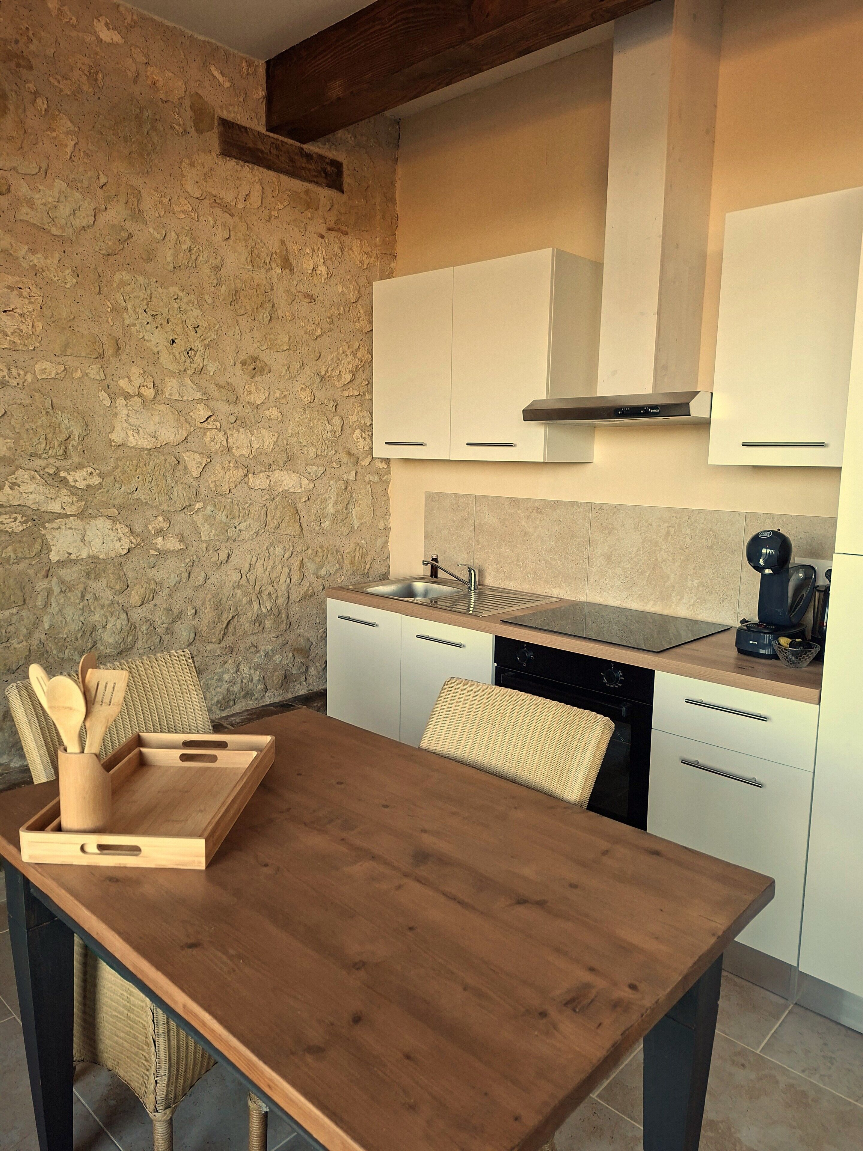 A kitchen with white cabinets, a wooden table, and a stone wall.