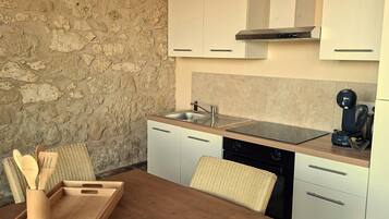 A kitchen with white cabinets, a wooden table, and a stone wall.