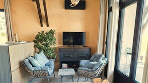 A cozy living room with a wooden dining table, two blue cushioned chairs, a TV on a dark cabinet, and a hanging light fixture. - Que Pour 2, Cottage/studio Le Bonheur, 1-bedroom with swimming pool and AC  Gers (Mauroux)