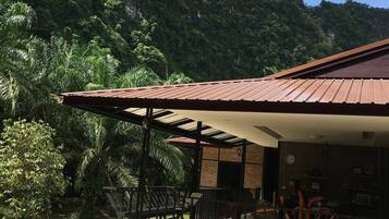 A building with a metal roof and brick walls, surrounded by lush greenery and a mountainous backdrop.