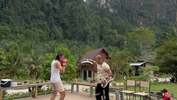 A tiled patio area with benches and a small building, surrounded by lush greenery and mountains in the background.