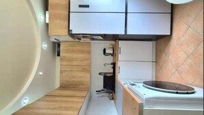 Une cuisine de taille réduite, dotée de meubles en bois, d’un lave-linge, d’un réfrigérateur et d’un évier.
