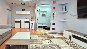 Un salon moderne avec un canapé, une table basse et un tapis à motifs. On y trouve également un coin cuisine avec des placards et une table à manger.