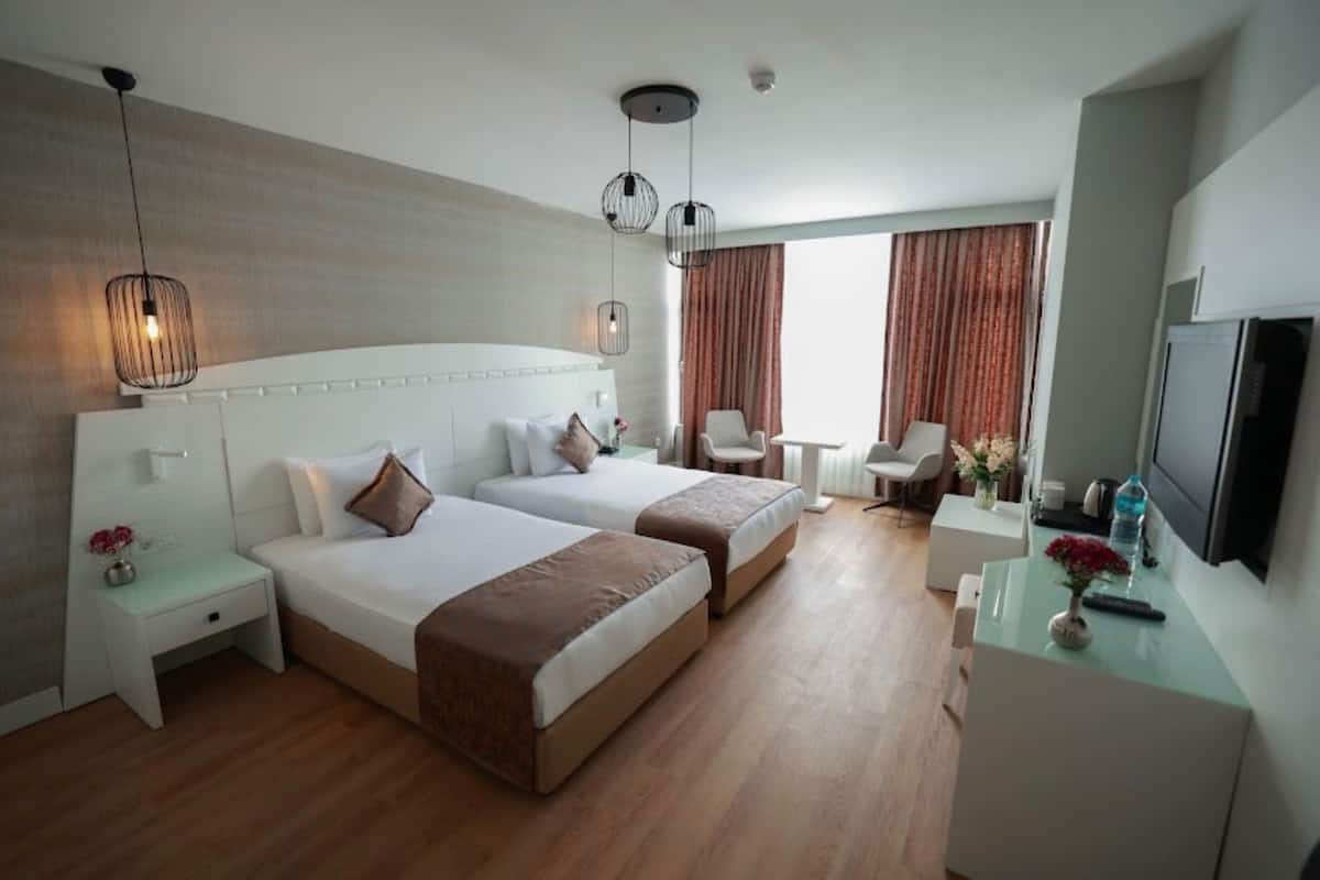 A modern hotel room with two beds, a desk, and a TV.