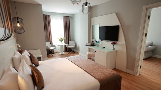 A hotel room with a large bed, a desk with a flat-screen TV, a chair, and a small table with flowers. - GOLDEN PARK HOTEL (İstanbul)