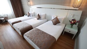 A hotel room with two beds, a small desk, a chair, and a nightstand with a vase of flowers. - GOLDEN PARK HOTEL (İstanbul)