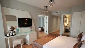 A modern hotel room with a large bed, a desk with a flat-screen TV, a small stool, and a walk-in closet. - GOLDEN PARK HOTEL (İstanbul)
