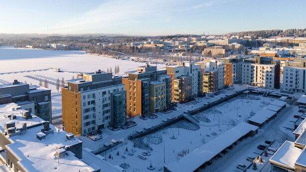 Een hoog wooncomplex met meerdere appartementencomplexen, een parkeerplaats en een groot open gebied op de voorgrond.