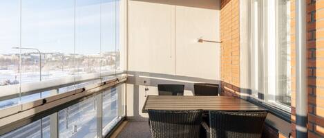 A balcony with a table and chairs, a view of a snowy landscape, and a brick wall.