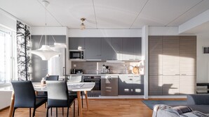 Een moderne keuken met grijze kastjes, een magnetron en een koffiezetapparaat. Er is een eethoek met een tafel en stoelen.